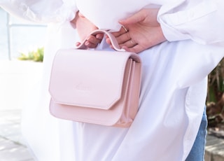 person in white dress shirt holding pink leather sling bag