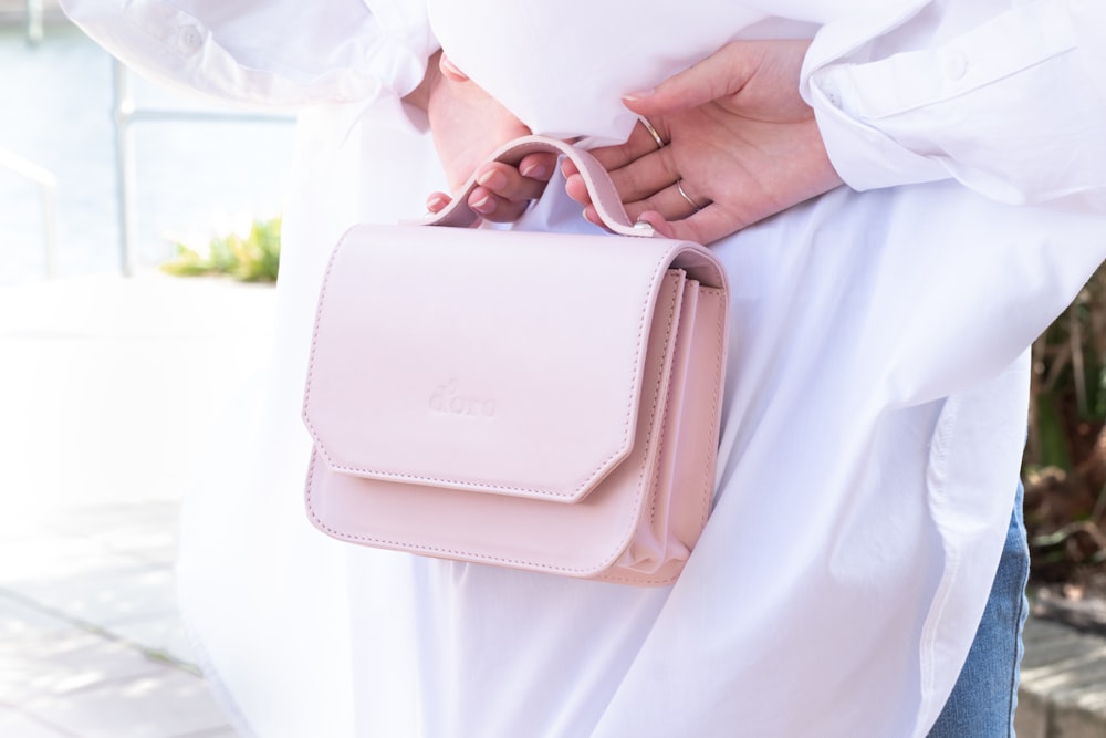 person in white dress shirt holding pink leather sling bag