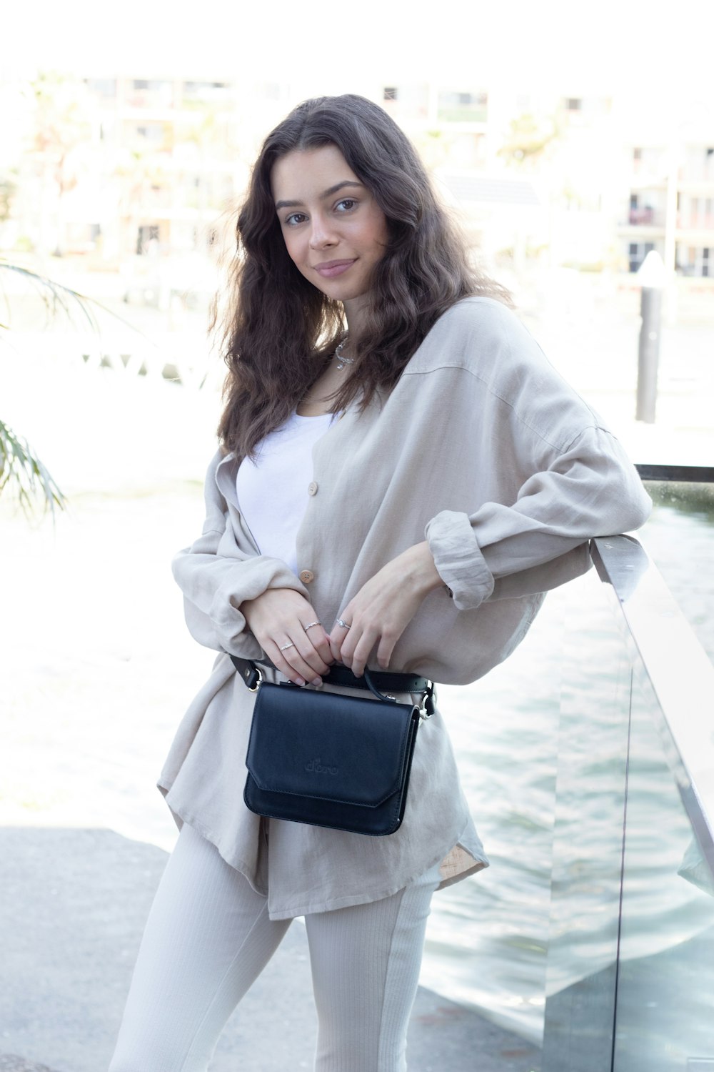 woman in white coat holding black leather sling bag