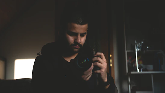 A moody portrait of the videographer focusing intensely behind the camera in a dim studio setting.