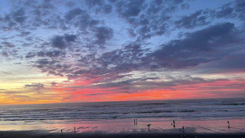A vibrant sunset over Bacnotan beach with surfers carrying their boards along the shore.