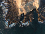 Close-up drone view of a coastal cliff with waves crashing below.
