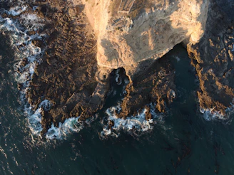 Aerial view of a coastal cliff with waves crashing below, captured by drone.