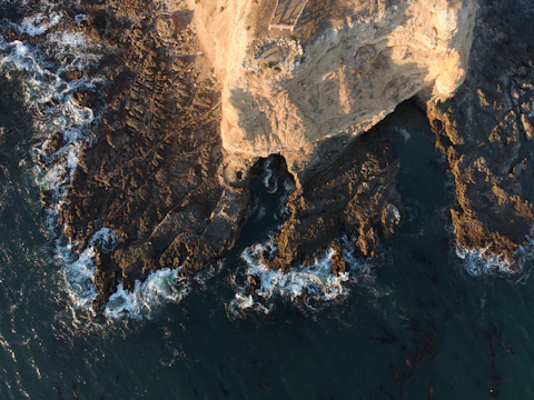 Close-up drone view of a coastal cliff with waves crashing below.