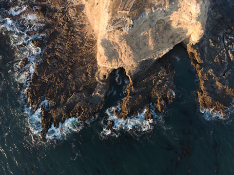 Aerial view of a coastal cliff with waves crashing below, captured by drone.