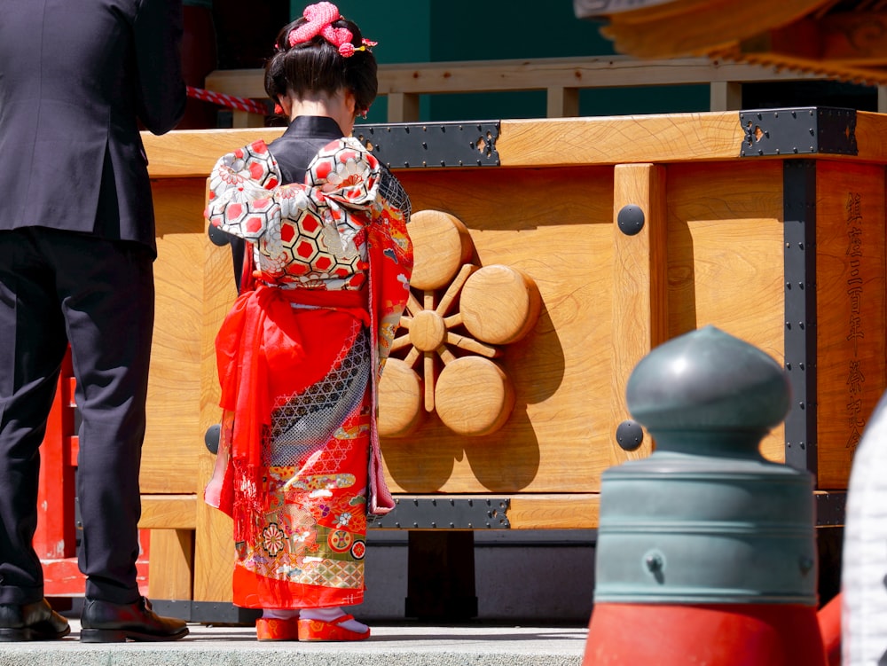 woman in red and white kimono standing near brown wooden bench