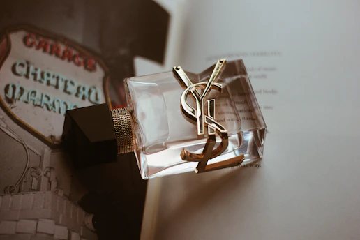 Close-up of a dark glass bottle with gold accents surrounded by fragrance ingredients.