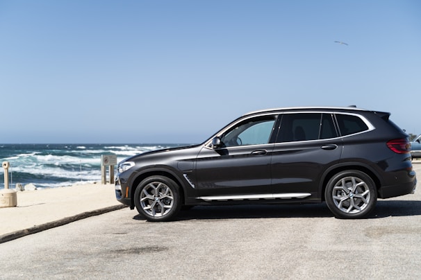 A spotless black SUV parked in front of a beach at sunset, reflecting the sky.