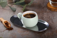 A steaming cup of coffee on a vintage ceramic saucer, surrounded by coffee beans and a small wooden spoon.