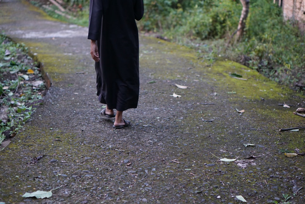 낮에 회색 콘크리트 통로를 걷는 검은 드레스를 입은 여자