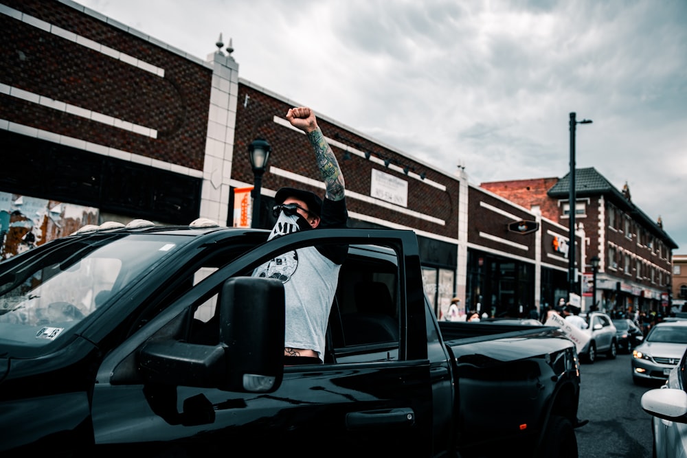 man in black jacket standing in front of black crew cab pickup truck during daytime