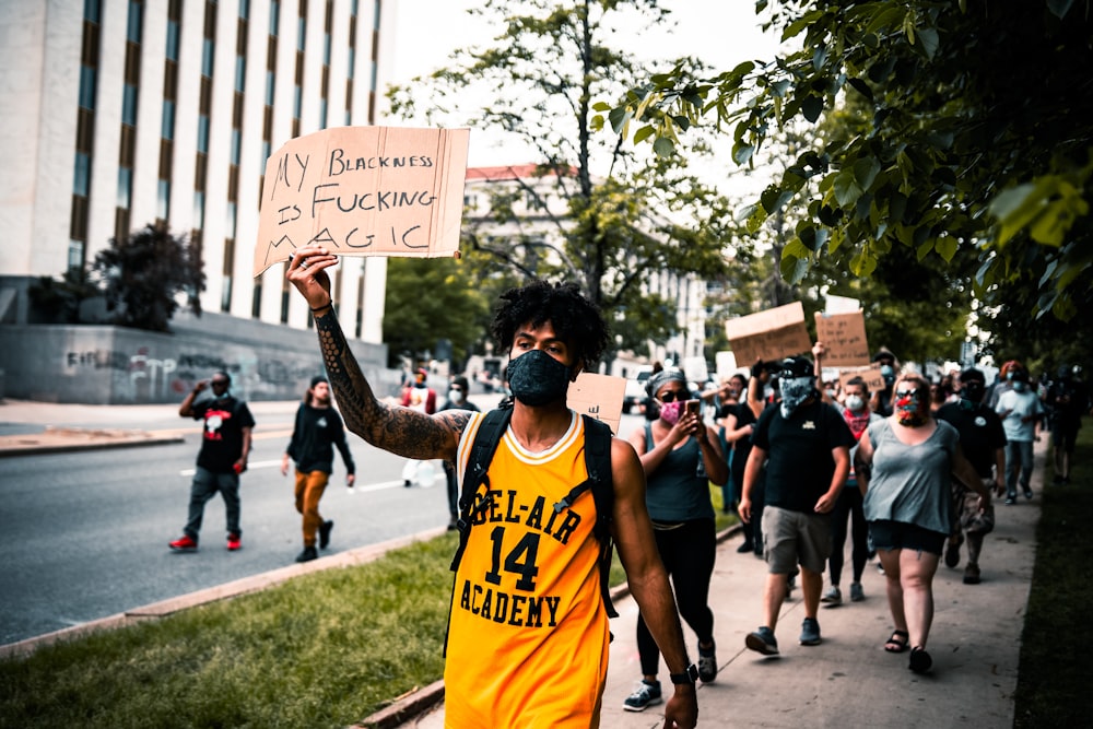man in yellow tank top holding white and black signage