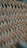 A close-up view of a woven material with a crisscross pattern made from thin, slightly curved strips of wood. The image captures the intricate details and texture of the weave with a shallow depth of field, blurring the background.