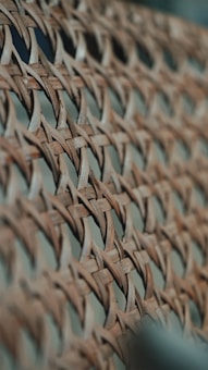 A close-up view of a woven material with a crisscross pattern made from thin, slightly curved strips of wood. The image captures the intricate details and texture of the weave with a shallow depth of field, blurring the background.