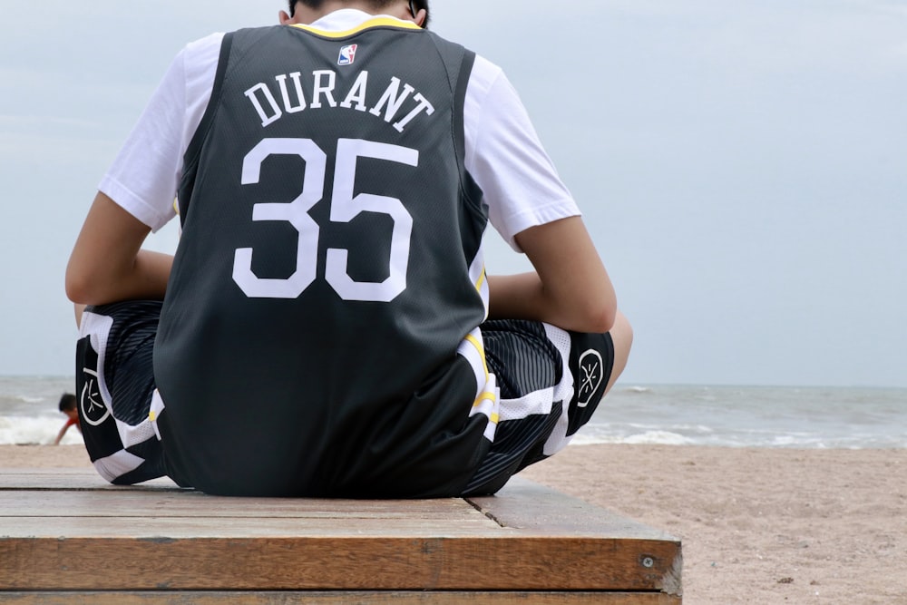 man in black and white jersey shirt sitting on brown wooden bench