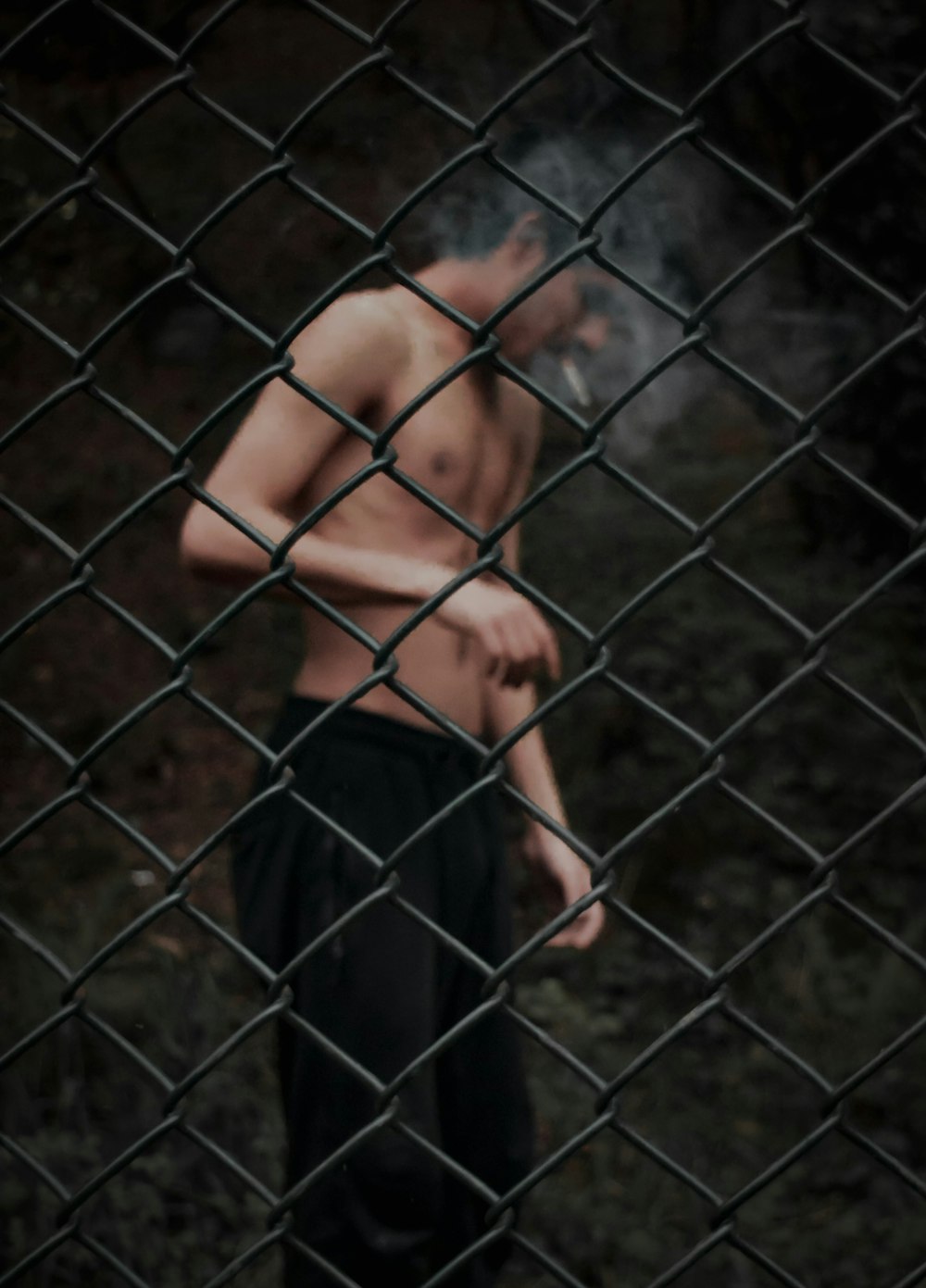 topless man in blue pants standing beside gray metal fence