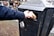 A hand is placing a disposable cup into a black outdoor trash bin on a cobblestone street. The trash bin is labeled with a graphic of a person throwing trash.