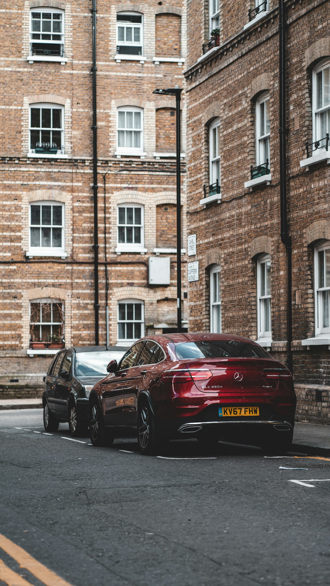 red sedan parked beside brown building during daytime
