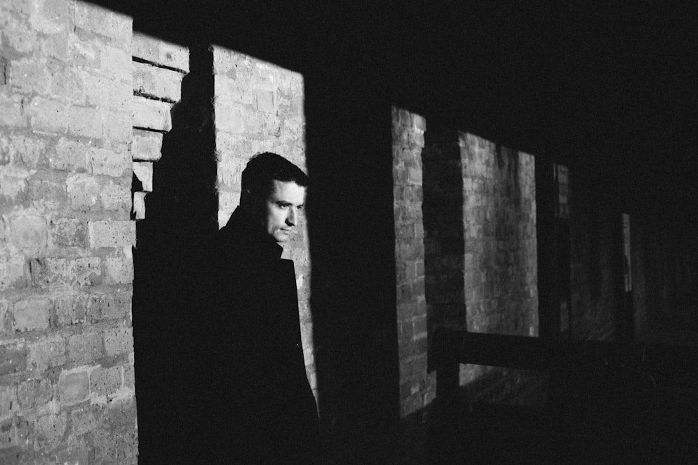 man in black suit standing near brick wall