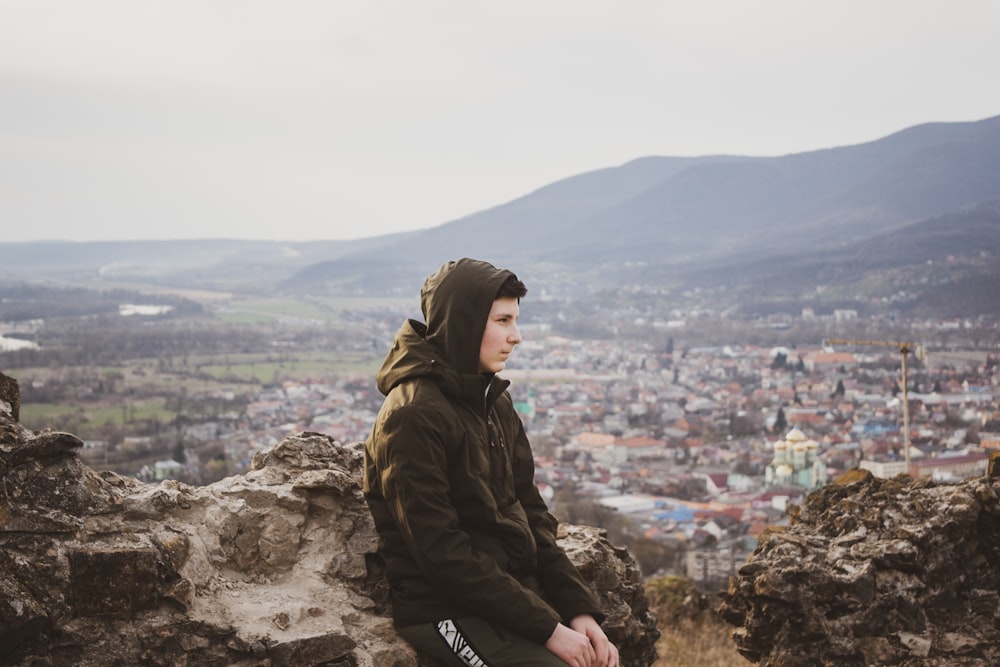 woman in black jacket sitting on rock during daytime