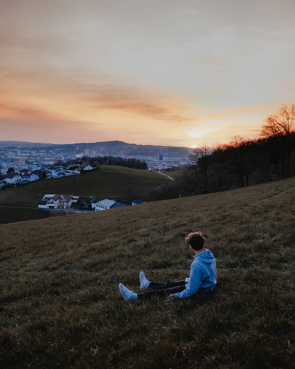 man in white hoodie sitting on green grass field during daytime