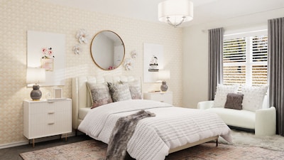 A cozy bedroom with a contemporary design featuring a large bed with textured bedding and several cushions. A round mirror is mounted on the wall above the headboard, flanked by decorative flowers. Two bedside tables with lamps add symmetry, and a plush white chair with pillows sits near the window. Natural light filters through gray curtains and white blinds, complementing the calming color palette of creams and grays.