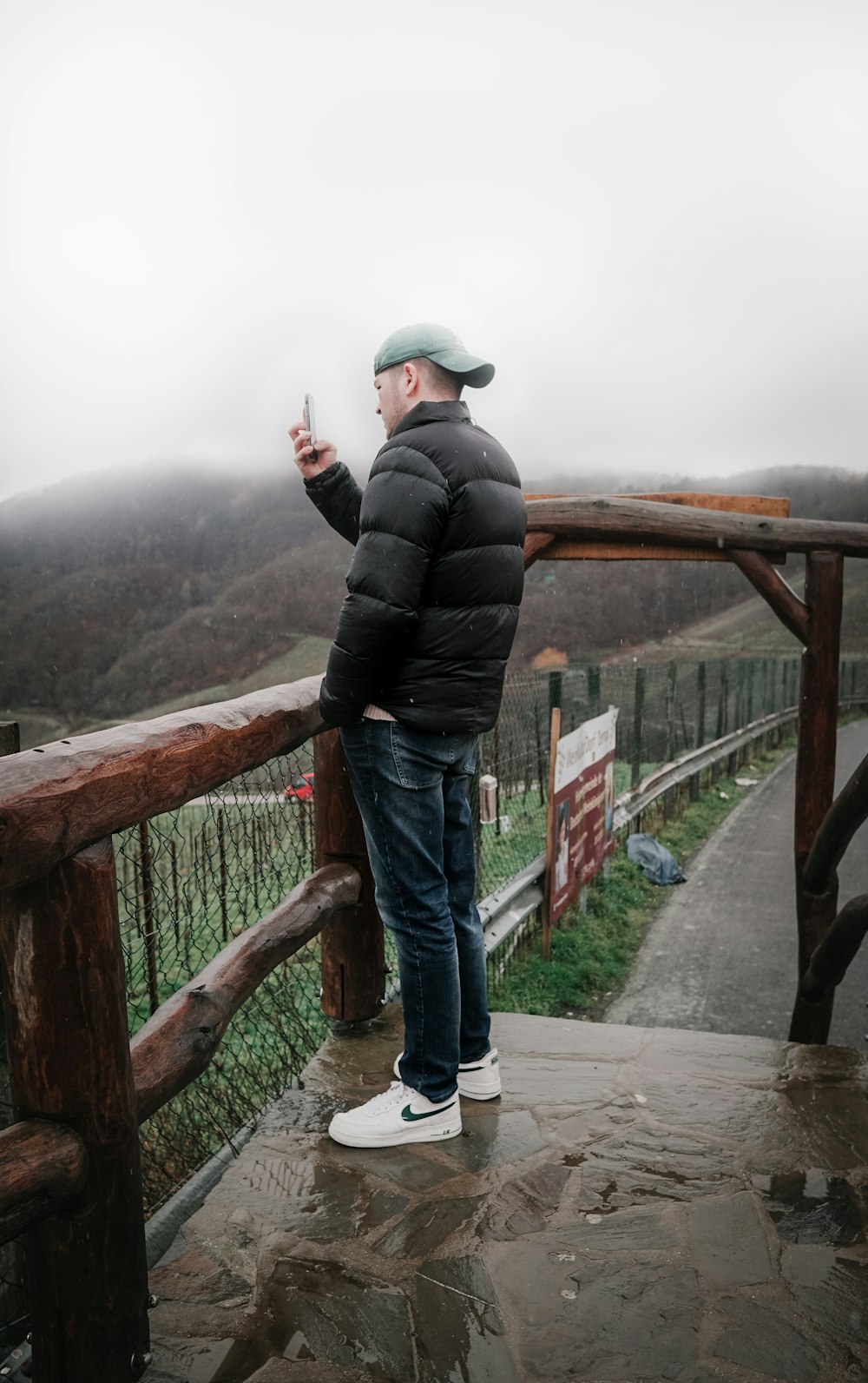 man in black jacket and blue denim jeans standing on bridge during daytime