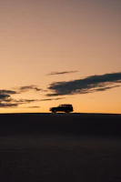 Sunset silhouette of a Jeep on a hilltop overlooking a vast desert landscape.