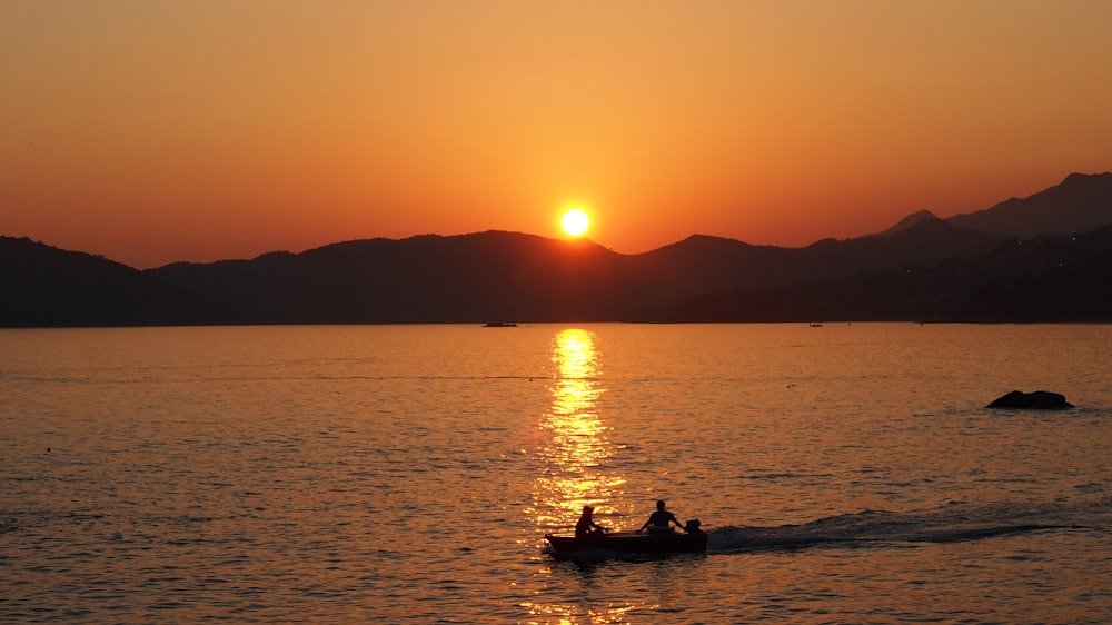 silhouette of 2 people riding boat on sea during sunset