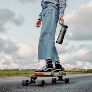 person in blue denim jeans and brown leather boots holding black and white bottle