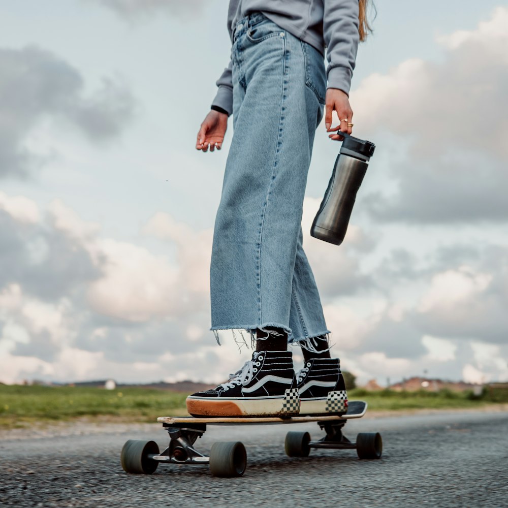 person in blue denim jeans and brown leather boots holding black and white bottle