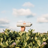 Hands holding a filled water bottle outdoors with green foliage background.