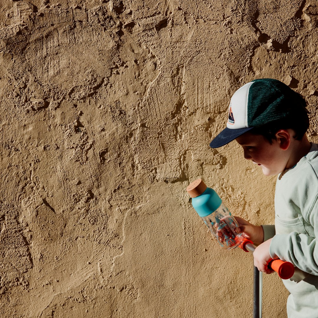 boy in white long sleeve shirt and black hat holding white and pink plastic bottle