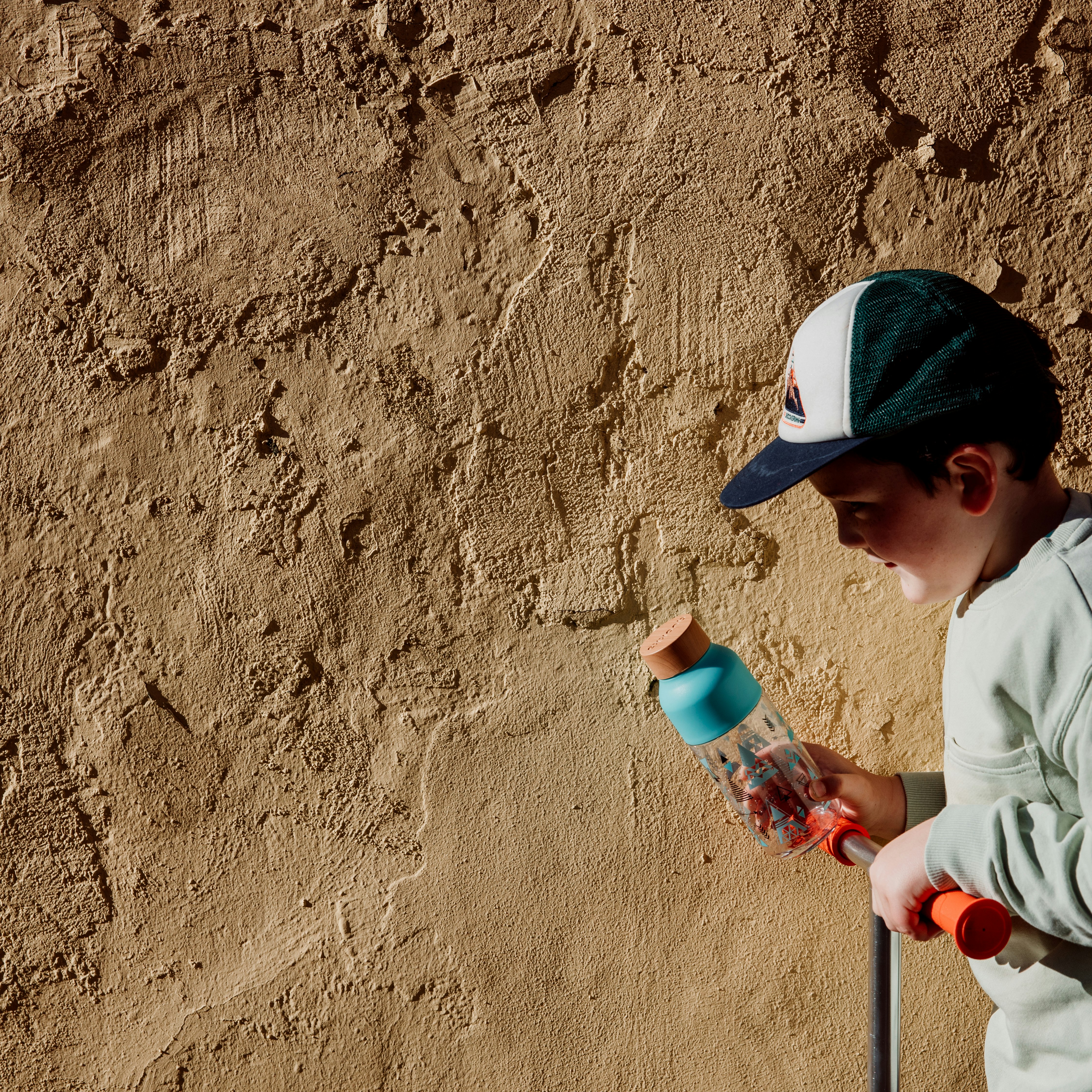 boy in white long sleeve shirt and black hat holding white and pink plastic bottle