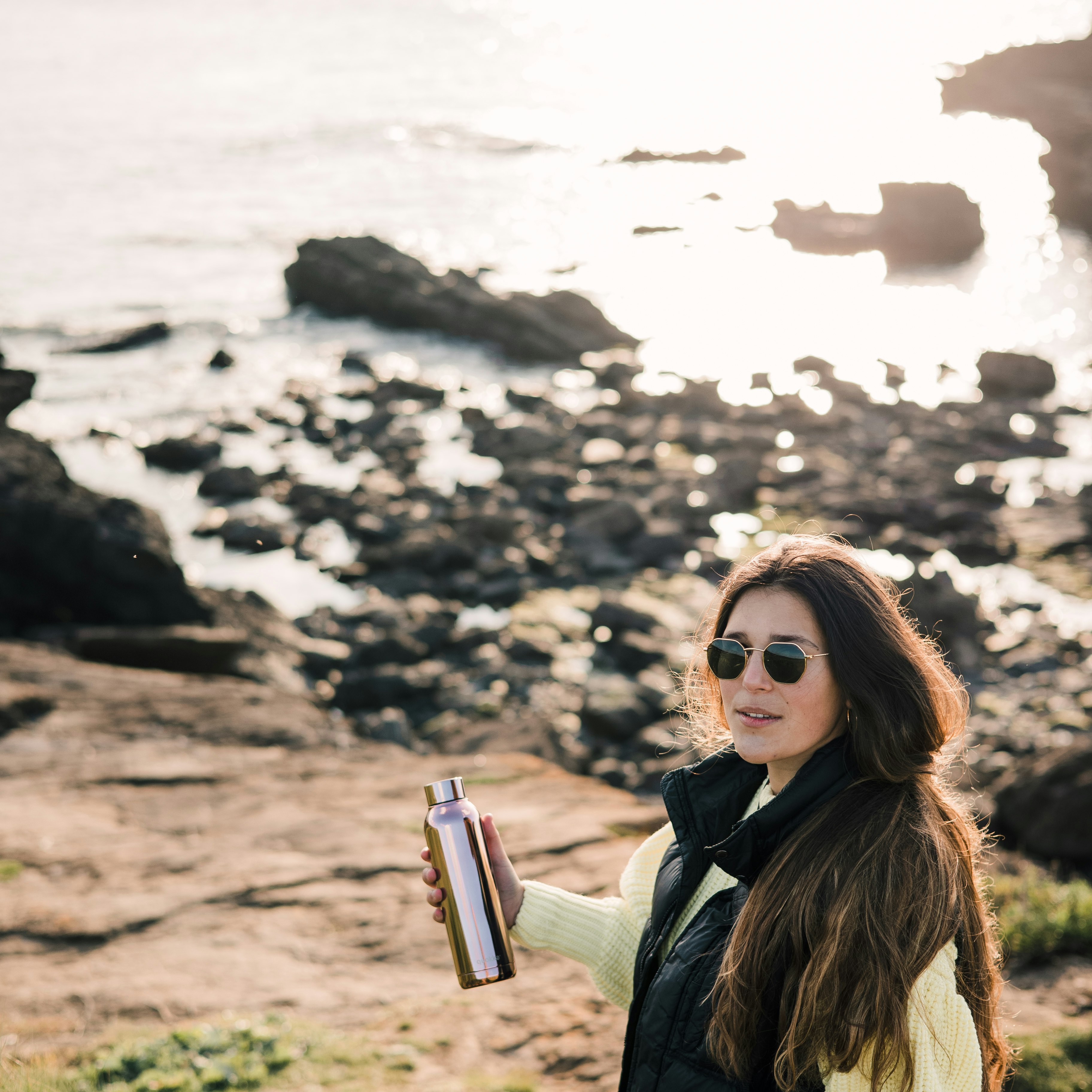 woman in black jacket holding tumbler near sea during daytime