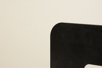 A minimalist image featuring a sharply defined black shape with rounded edges against a plain beige background. The shape occupies the right side, creating a stark contrast.