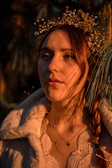 Elegant woman wearing a golden laurel crown necklace, glowing under vibrant warm light.