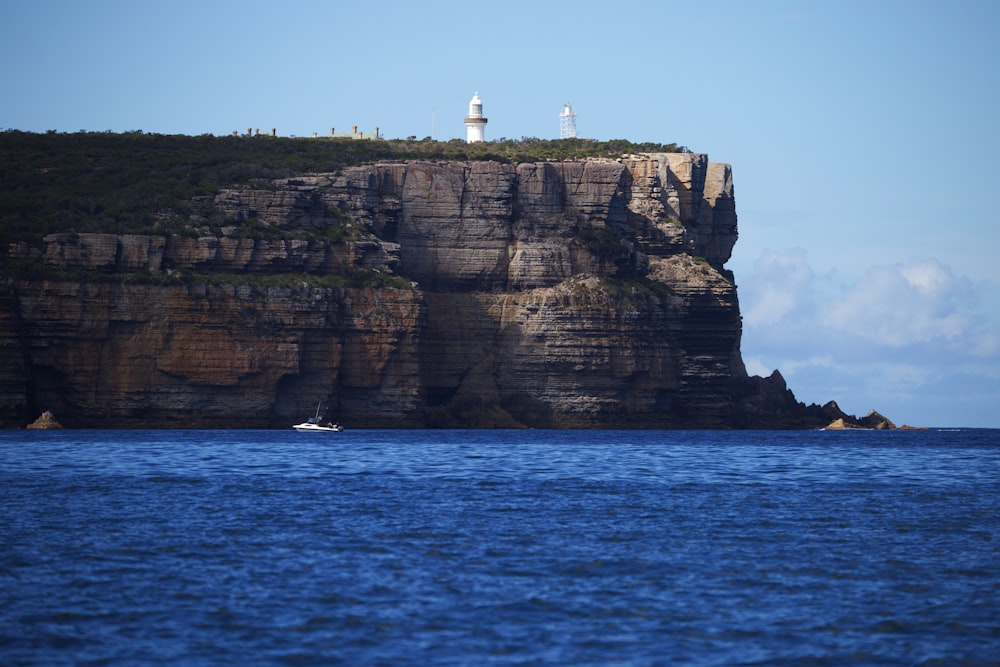 Weißer Leuchtturm auf brauner Felsformation in der Nähe von Gewässern tagsüber