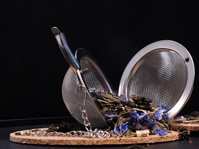 An elegant stainless steel tea infuser resting on a ceramic dish.