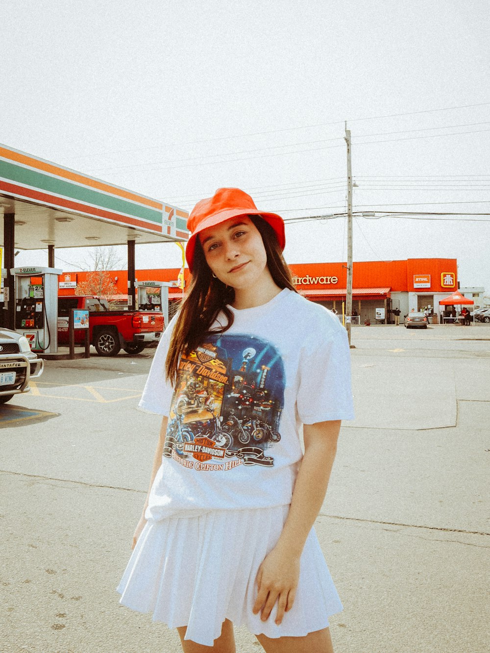 woman in white crew neck t-shirt and red hat standing on sidewalk during daytime