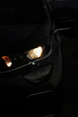 Close-up shot of Mazda3’s headlight reflecting soft ambient light in a dark setting.