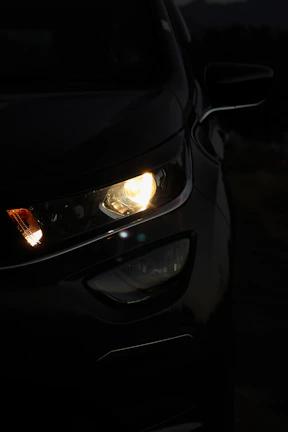 Close-up shot of Mazda3’s headlight reflecting soft ambient light in a dark setting.