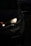 A close-up view of a car's front headlight illuminated in the dark. The light casts a soft glow, highlighting the sleek contours of the vehicle. The surrounding environment is dimly lit, adding to the contrast.