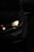 A close-up view of a car's front headlight illuminated in the dark. The light casts a soft glow, highlighting the sleek contours of the vehicle. The surrounding environment is dimly lit, adding to the contrast.