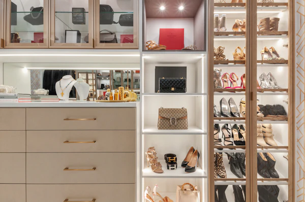 A boutique-style closet with lit glass cabinets for shoes and handbags
