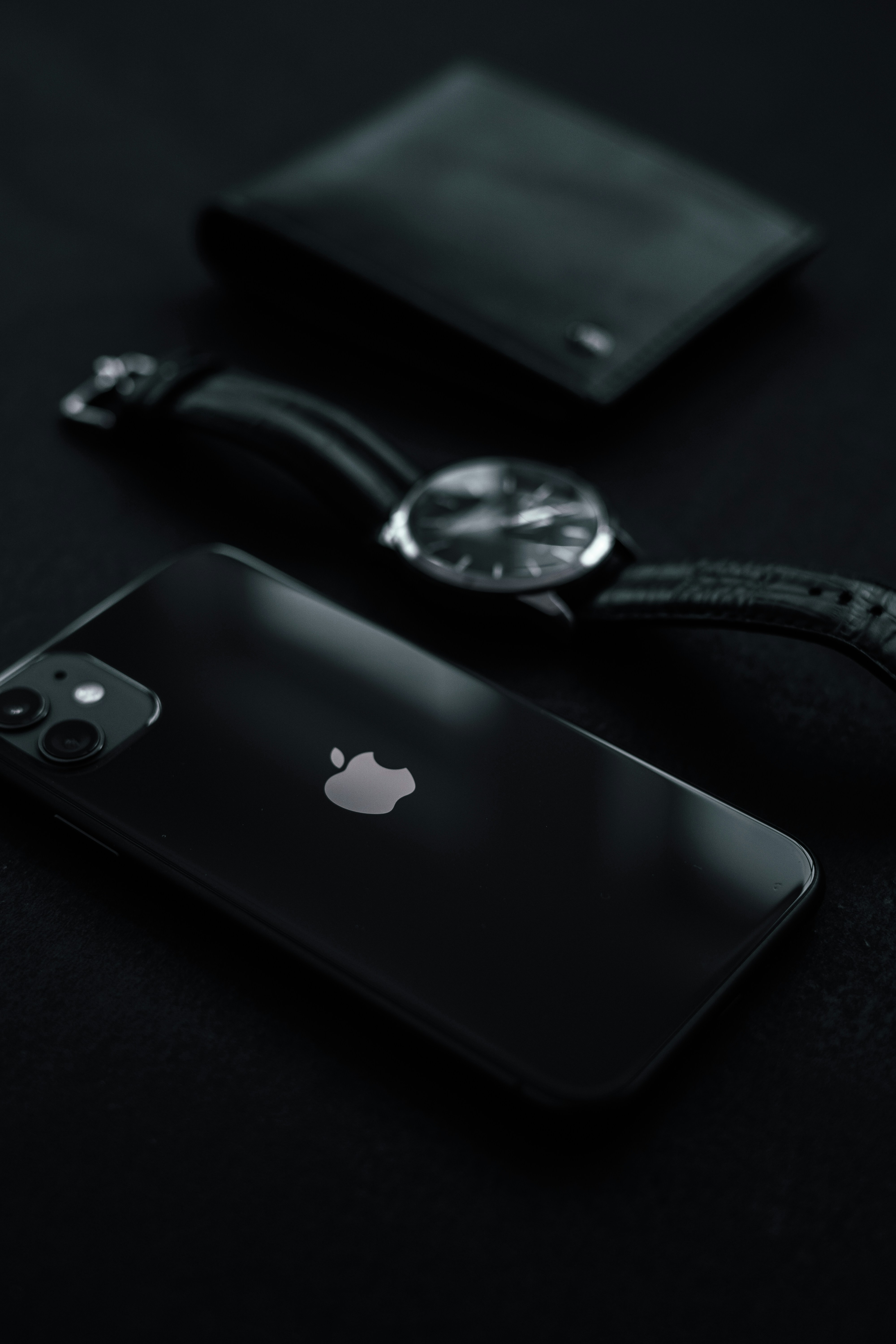 Luxury leather accessories — wallet, watch, and bracelet arranged on dark slate surface, dramatic side lighting