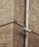 A corner of a brick building is featured with a surveillance camera mounted onto a vertical metal pipe. The bricks have a rough texture and are laid in a horizontal pattern. The camera is positioned at an angle, focused on the intersecting corner of the structure.