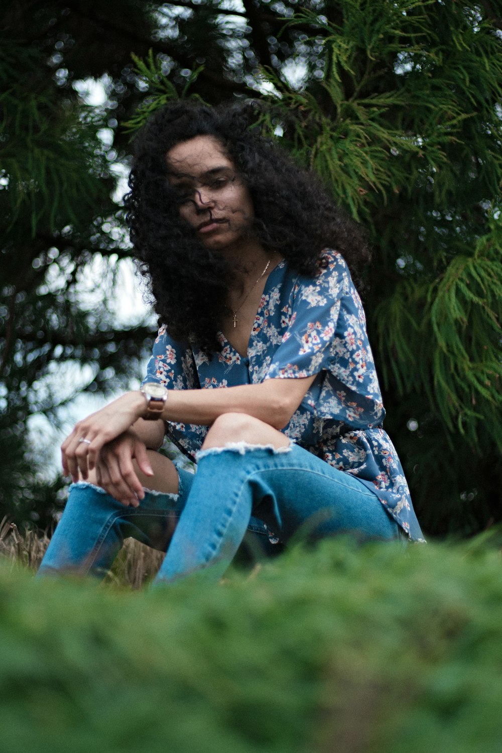 woman in blue and white floral shirt and blue denim jeans sitting on green grass during