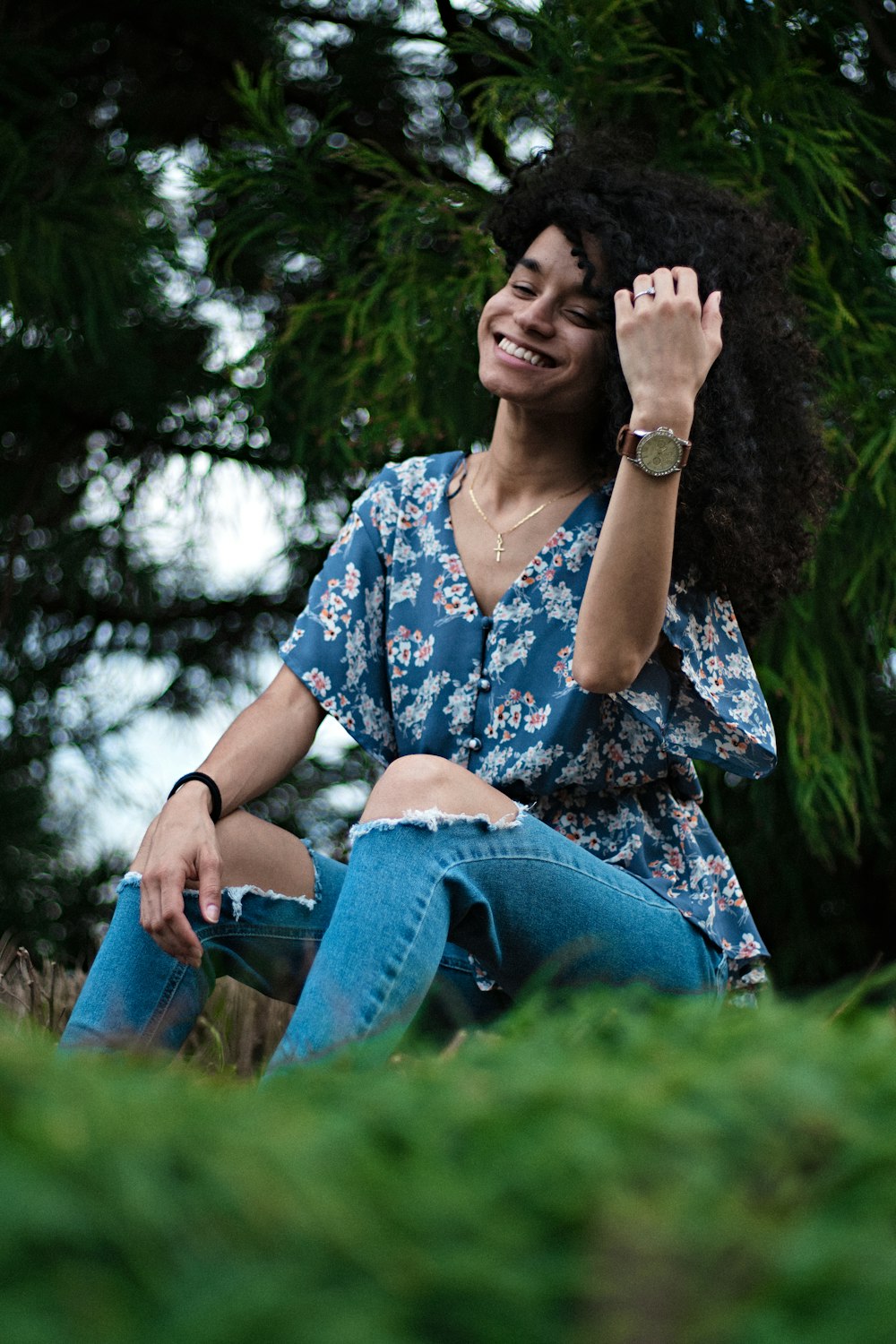 woman in blue and white floral shirt and blue denim jeans sitting on green grass during