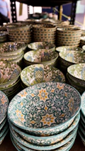 A collection of stoneware bowls in warm, cheerful hues arranged on a wooden shelf.